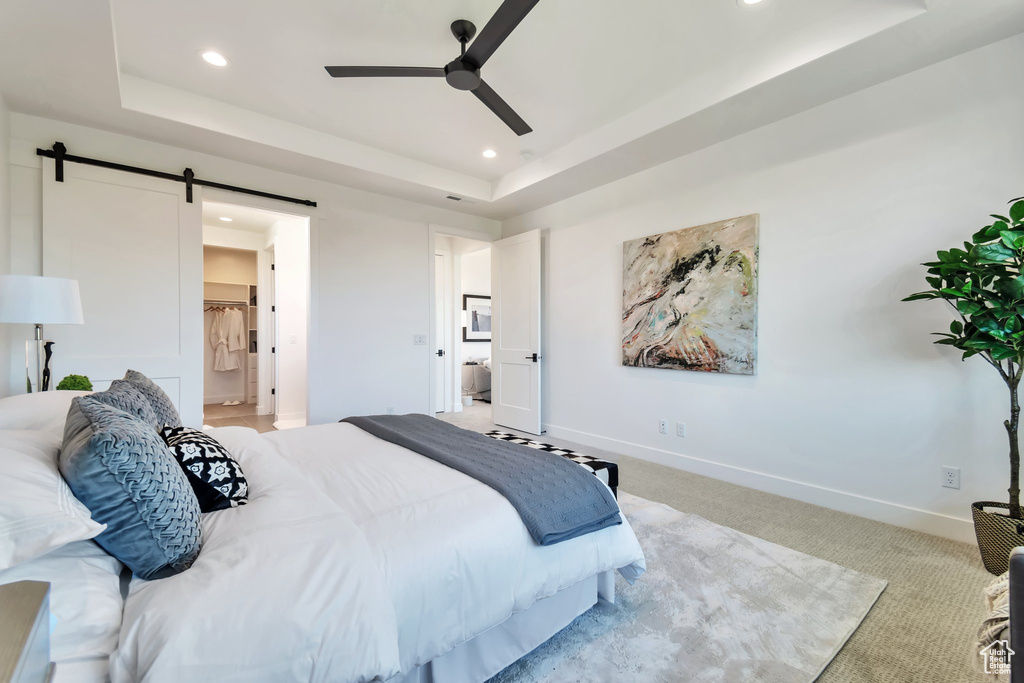 Bedroom featuring ensuite bath, a raised ceiling, light carpet, and a barn door