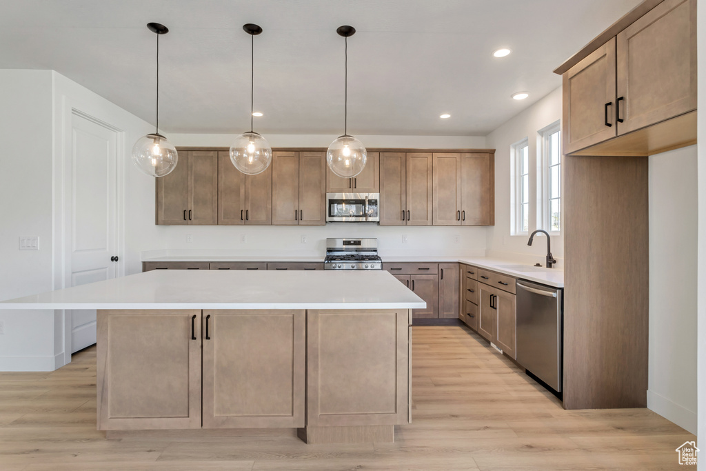Kitchen with decorative light fixtures, light hardwood / wood-style floors, a center island, and stainless steel appliances