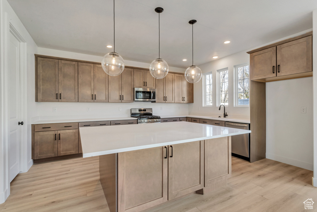 Kitchen with a kitchen island, light wood-type flooring, stainless steel appliances, and decorative light fixtures