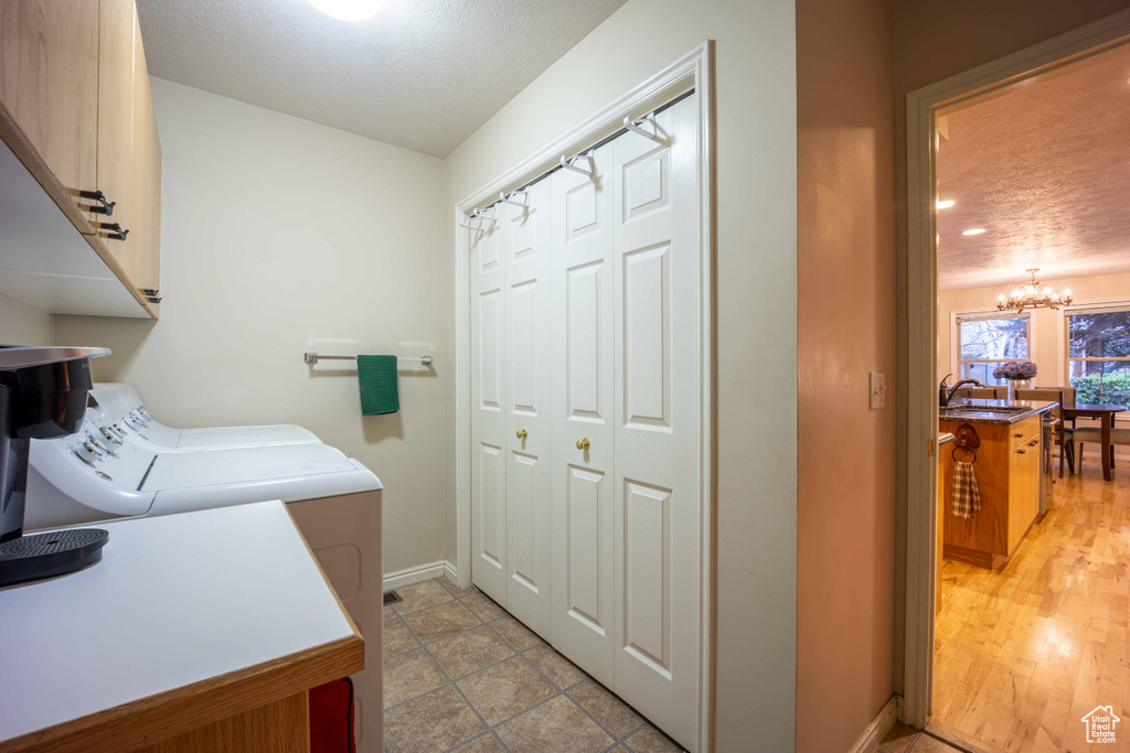 Laundry area with cabinets, washing machine and clothes dryer, sink, light tile flooring, and an inviting chandelier