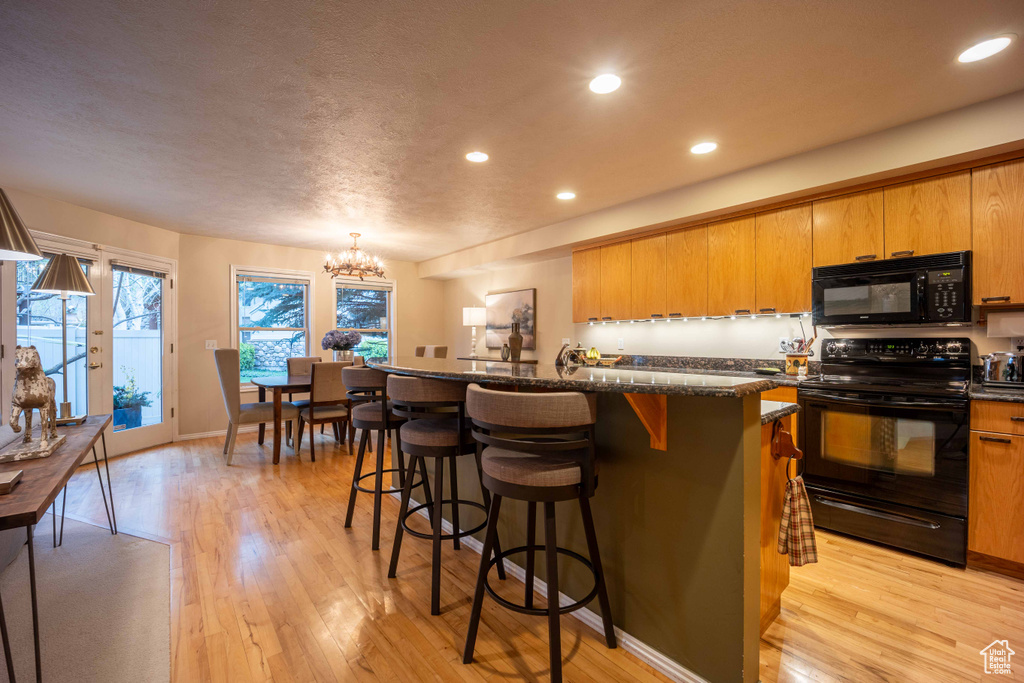 Kitchen with a center island, light wood-type flooring, a kitchen breakfast bar, and black appliances