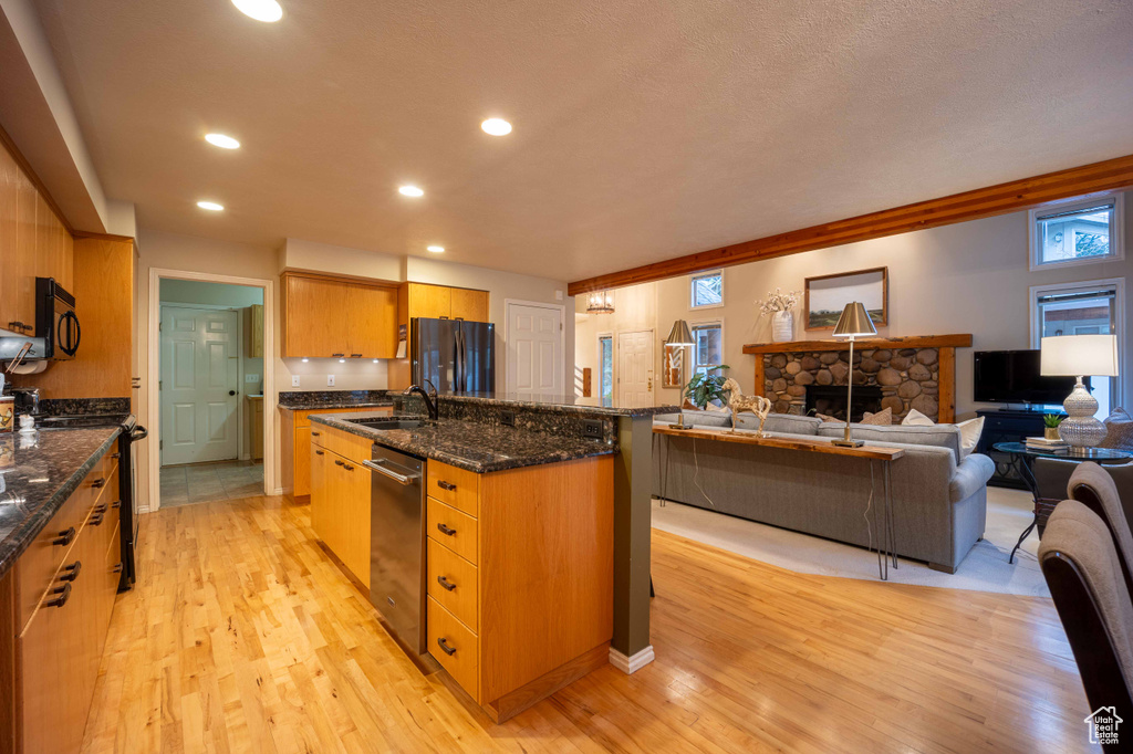 Kitchen featuring a fireplace, black appliances, light wood-type flooring, and a kitchen island with sink