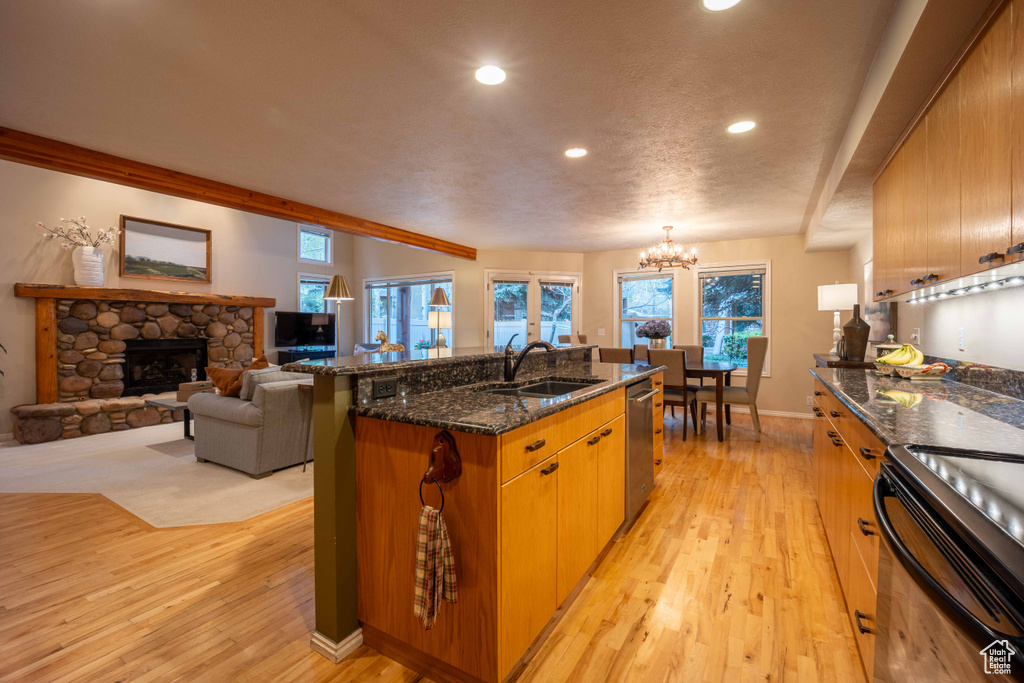 Kitchen with light hardwood / wood-style floors, a kitchen island with sink, sink, and a fireplace