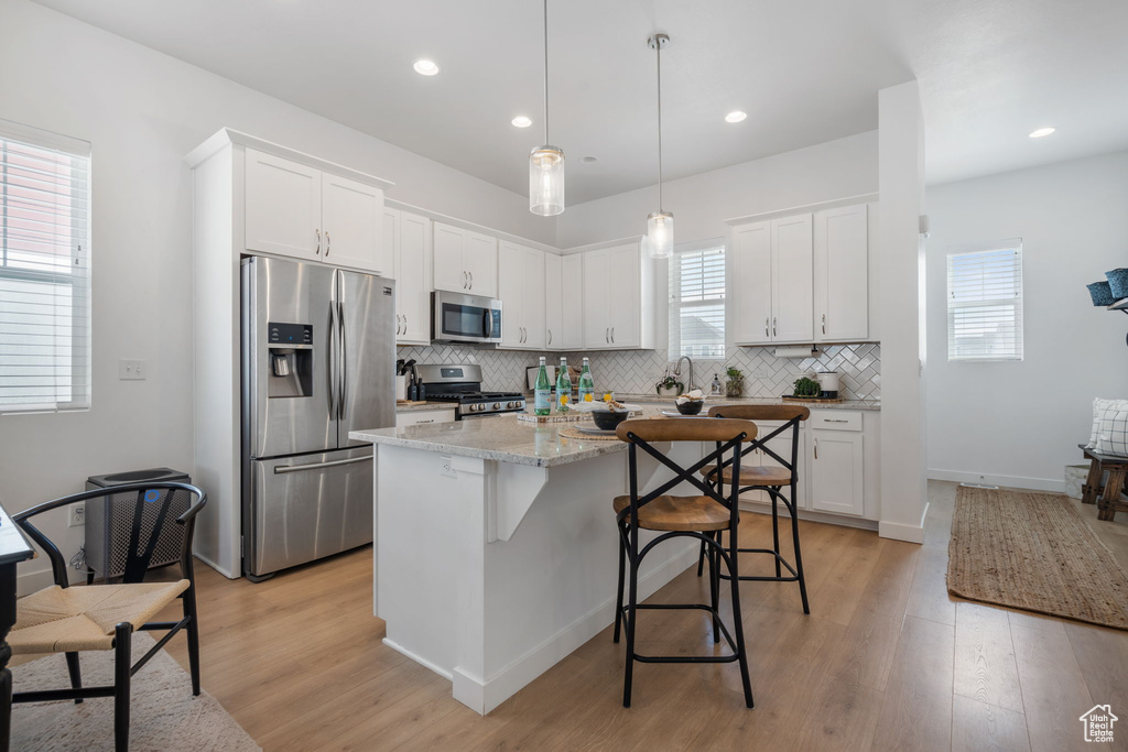 Kitchen with decorative light fixtures, appliances with stainless steel finishes, light hardwood / wood-style flooring, white cabinets, and a healthy amount of sunlight