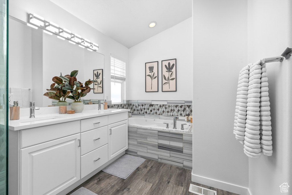 Bathroom featuring lofted ceiling, a relaxing tiled bath, hardwood / wood-style flooring, and double sink vanity