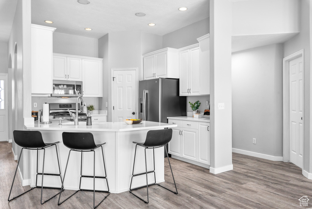 Kitchen featuring appliances with stainless steel finishes, light hardwood / wood-style floors, white cabinetry, sink, and a breakfast bar