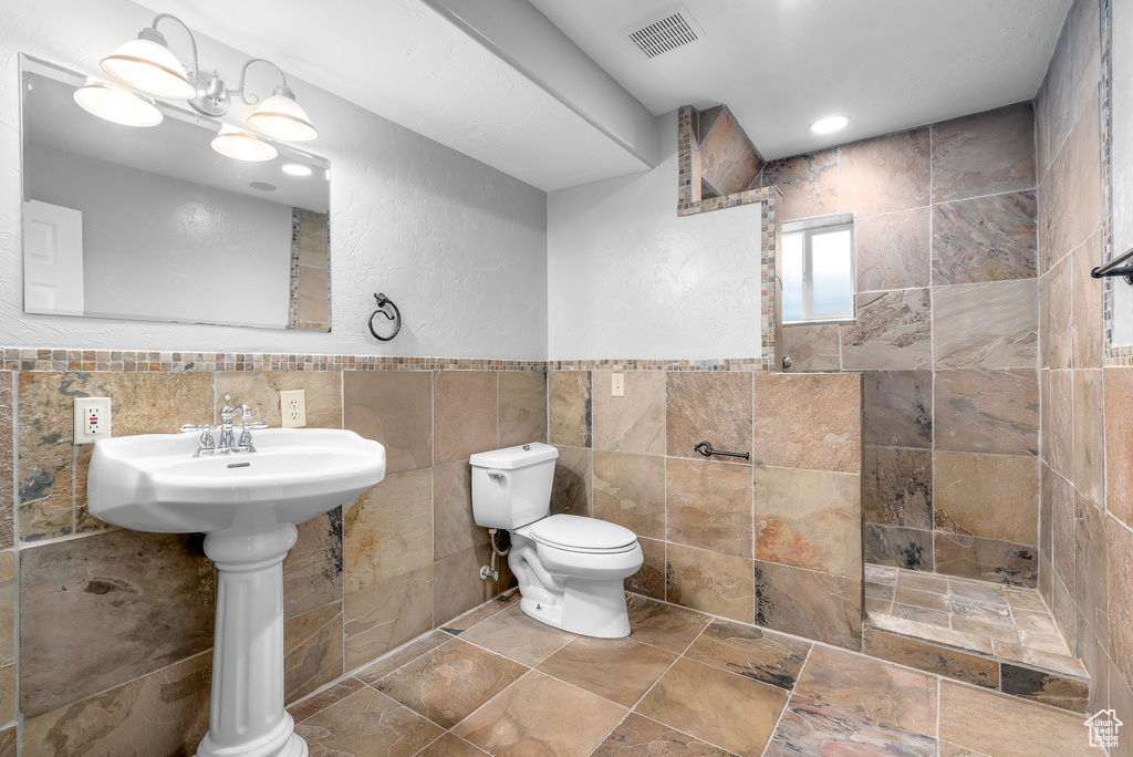 Bathroom featuring tile walls, a tile shower, toilet, tasteful backsplash, and a chandelier