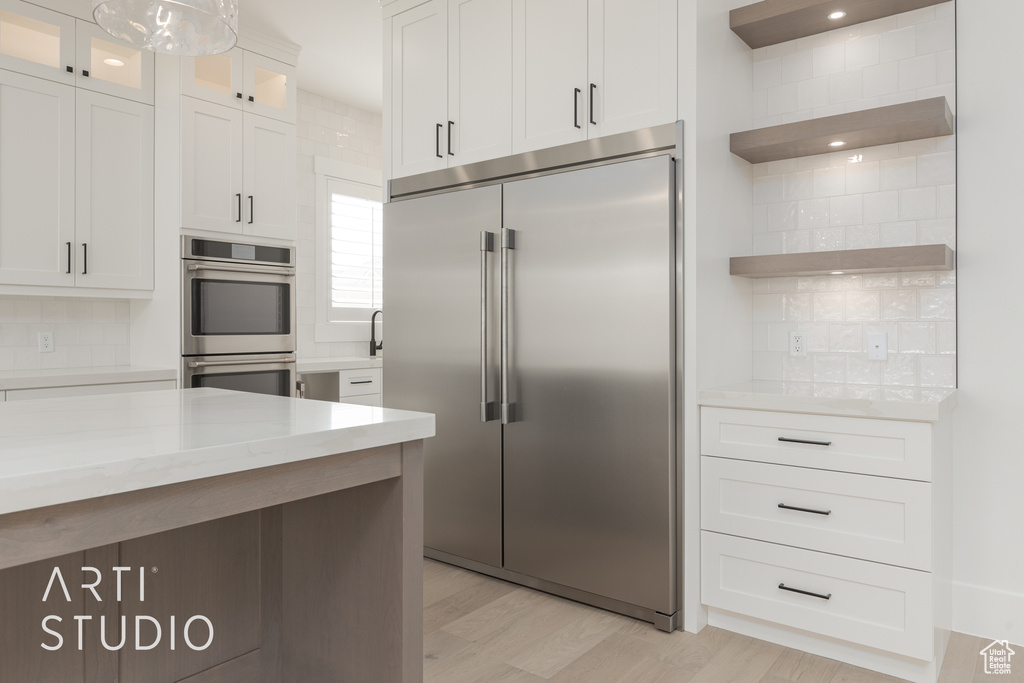 Kitchen featuring light stone countertops, light hardwood / wood-style flooring, stainless steel appliances, tasteful backsplash, and white cabinets