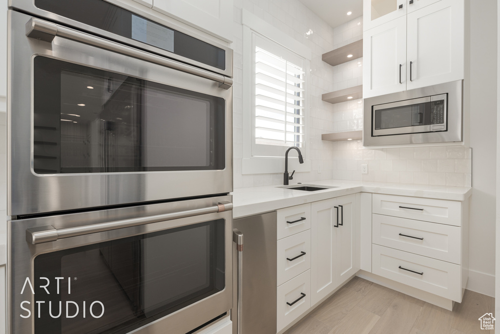 Kitchen featuring white cabinets, light wood-type flooring, backsplash, appliances with stainless steel finishes, and sink
