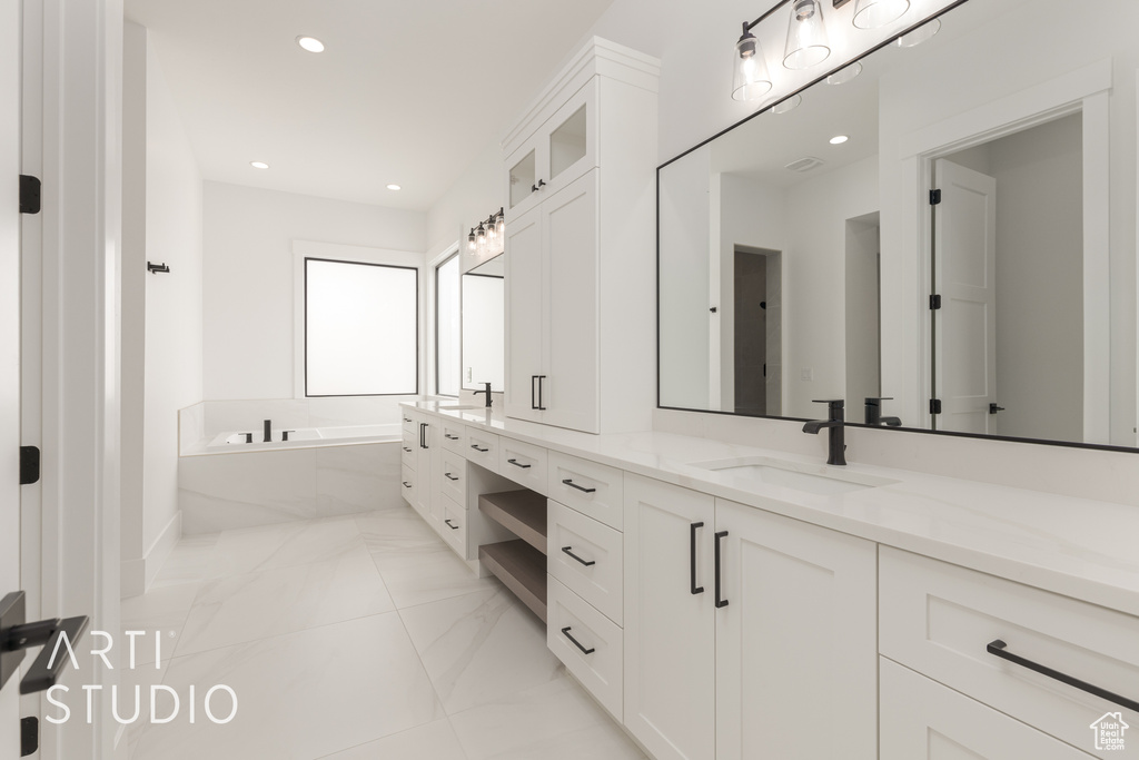 Bathroom featuring large vanity, tile floors, dual sinks, and tiled tub