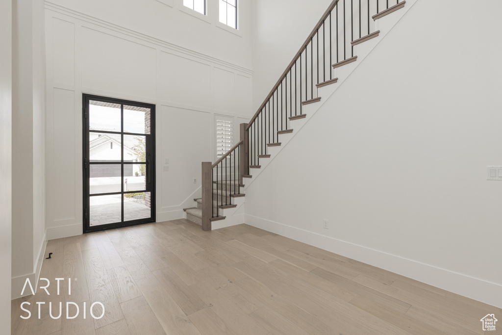 Foyer entrance with light hardwood / wood-style flooring, a towering ceiling, and a wealth of natural light