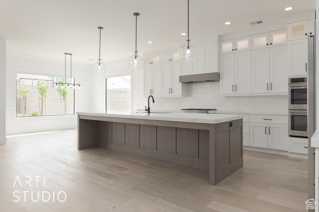 Kitchen with white cabinetry, backsplash, appliances with stainless steel finishes, sink, and an island with sink