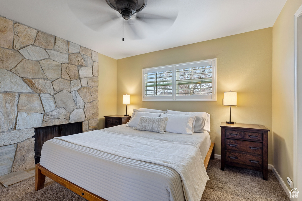 Carpeted bedroom featuring ceiling fan and a fireplace