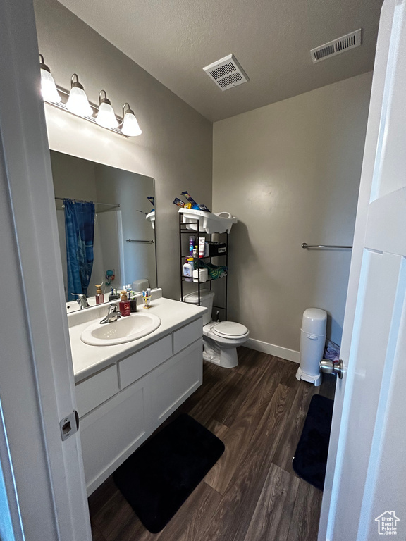 Bathroom featuring hardwood / wood-style flooring, toilet, oversized vanity, and a textured ceiling