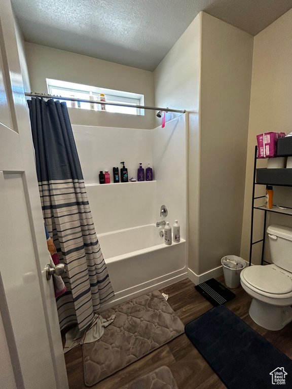 Bathroom featuring a healthy amount of sunlight, toilet, shower / bathtub combination with curtain, and hardwood / wood-style floors