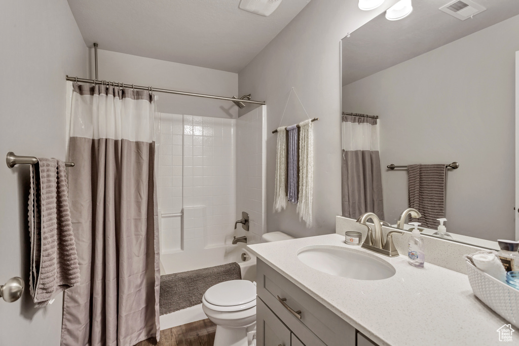Full bathroom with oversized vanity, hardwood / wood-style flooring, toilet, and shower / bathtub combination with curtain