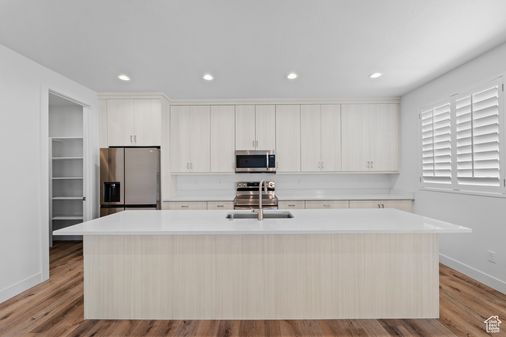 Kitchen featuring light hardwood / wood-style floors, stainless steel appliances, white cabinets, and a center island with sink