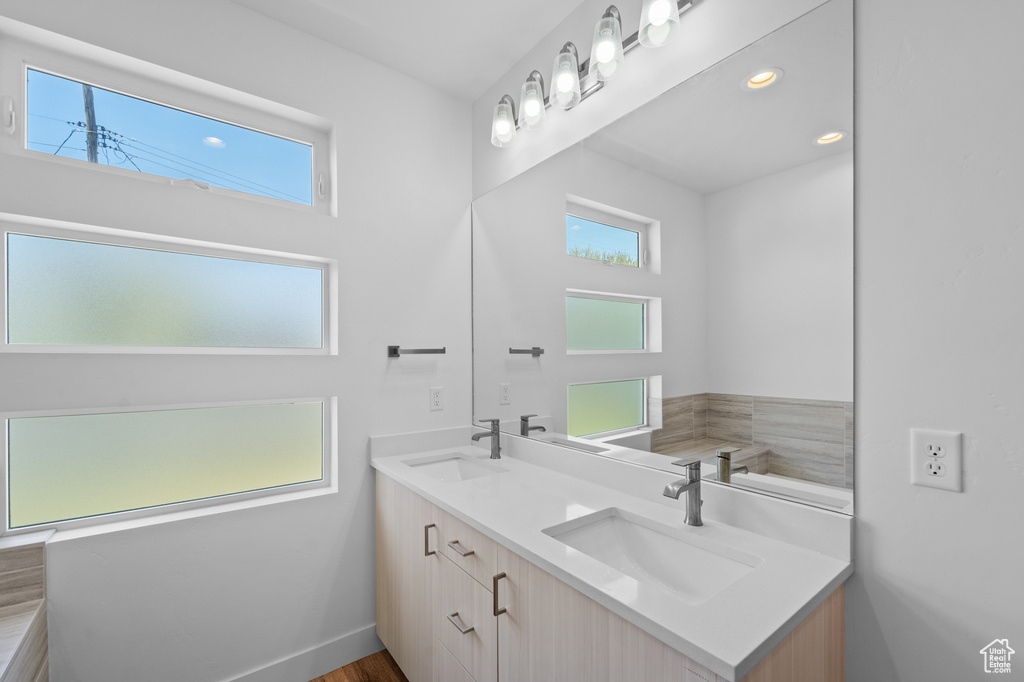 Bathroom with dual sinks, plenty of natural light, vanity with extensive cabinet space, and hardwood / wood-style flooring