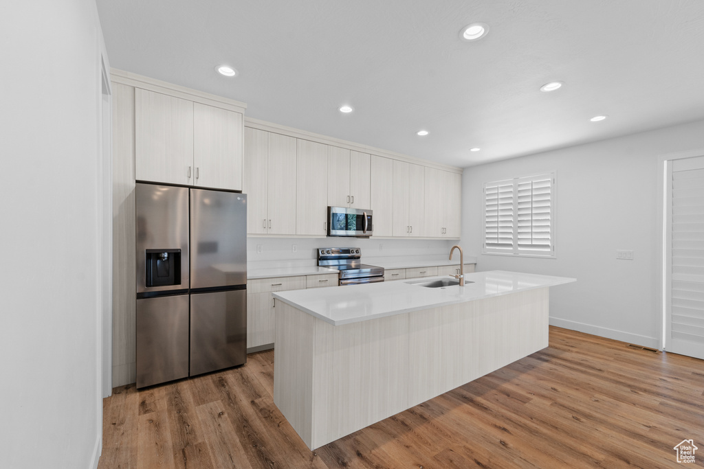 Kitchen featuring sink, stainless steel appliances, light hardwood / wood-style floors, and a kitchen island with sink