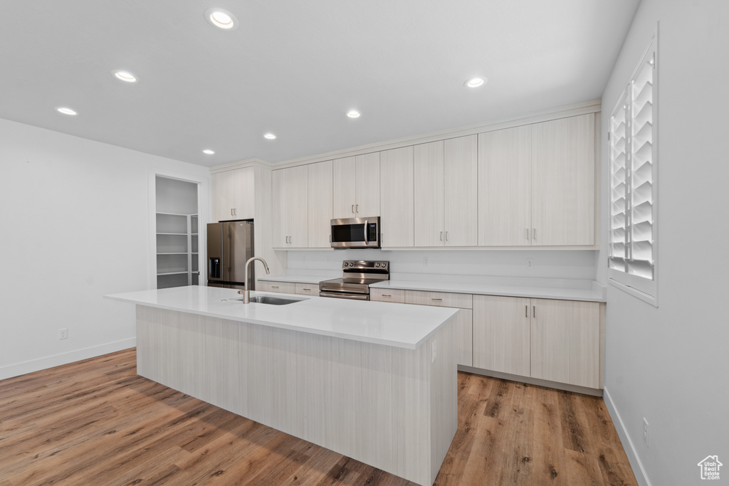 Kitchen featuring appliances with stainless steel finishes, white cabinets, sink, light hardwood / wood-style flooring, and a kitchen island with sink