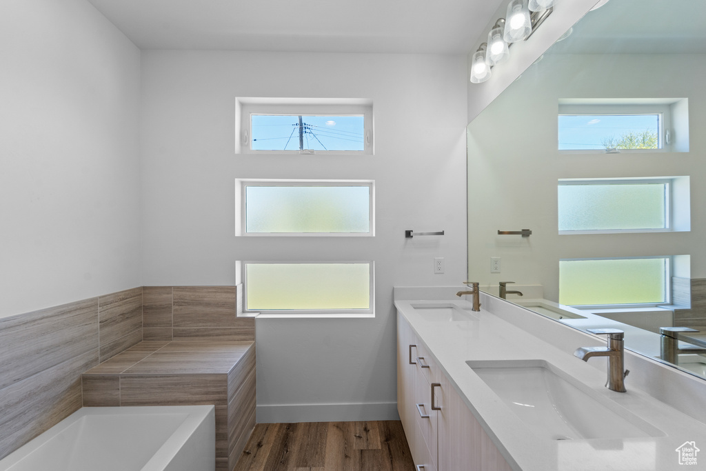 Bathroom with a wealth of natural light, a bath to relax in, hardwood / wood-style floors, and double sink vanity