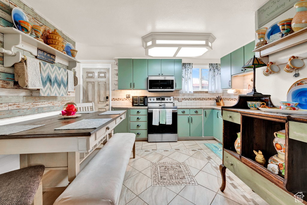 Kitchen featuring backsplash, light tile floors, green cabinetry, and range with electric stovetop