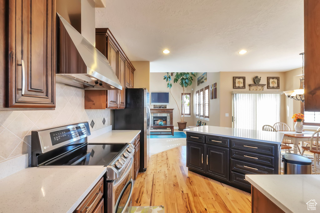 Kitchen featuring backsplash, wall chimney range hood, light wood-type flooring, electric range, and light stone countertops