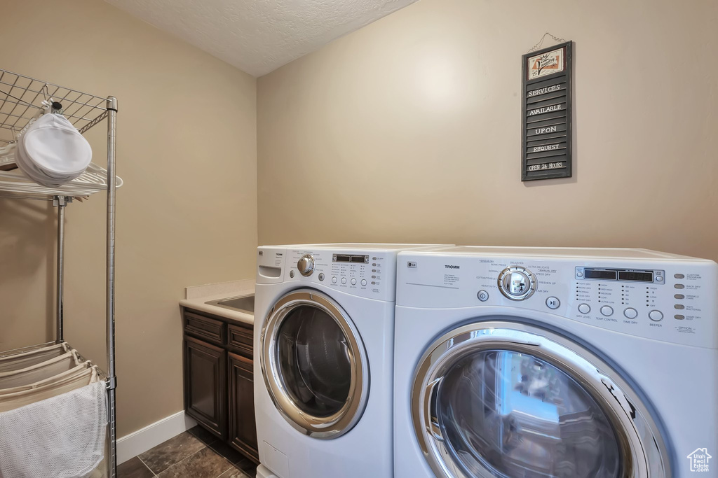 Laundry room with cabinets, a textured ceiling, washer and dryer, and dark tile floors