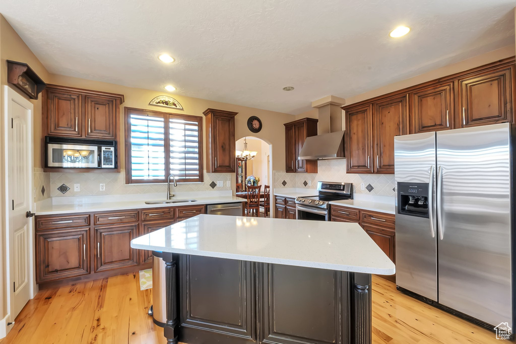Kitchen featuring appliances with stainless steel finishes, light hardwood / wood-style floors, wall chimney range hood, sink, and a breakfast bar