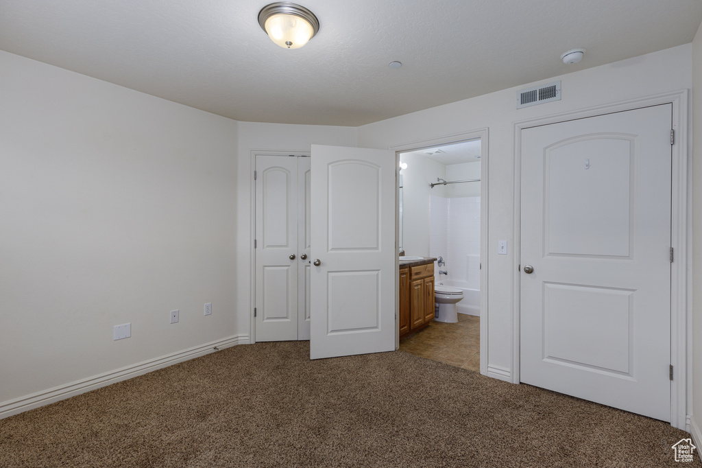 Unfurnished bedroom with connected bathroom, dark carpet, and a closet