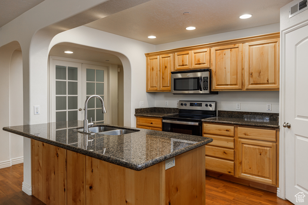 Kitchen featuring appliances with stainless steel finishes, a center island with sink, dark wood-type flooring, dark stone countertops, and sink