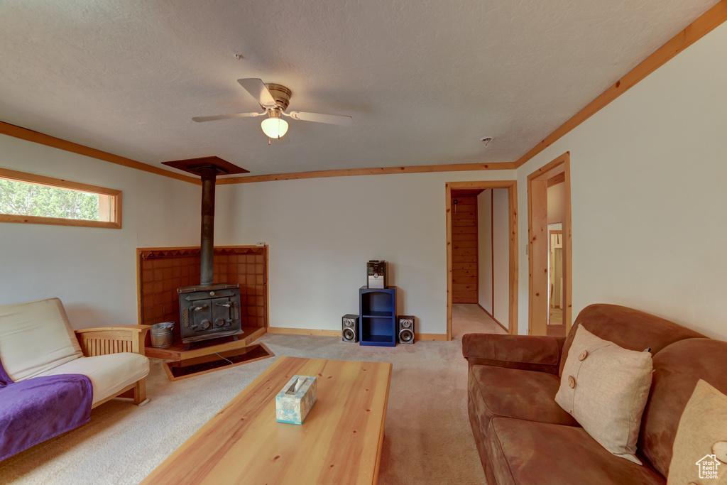 Carpeted living room featuring a textured ceiling, a wood stove, ceiling fan, and crown molding