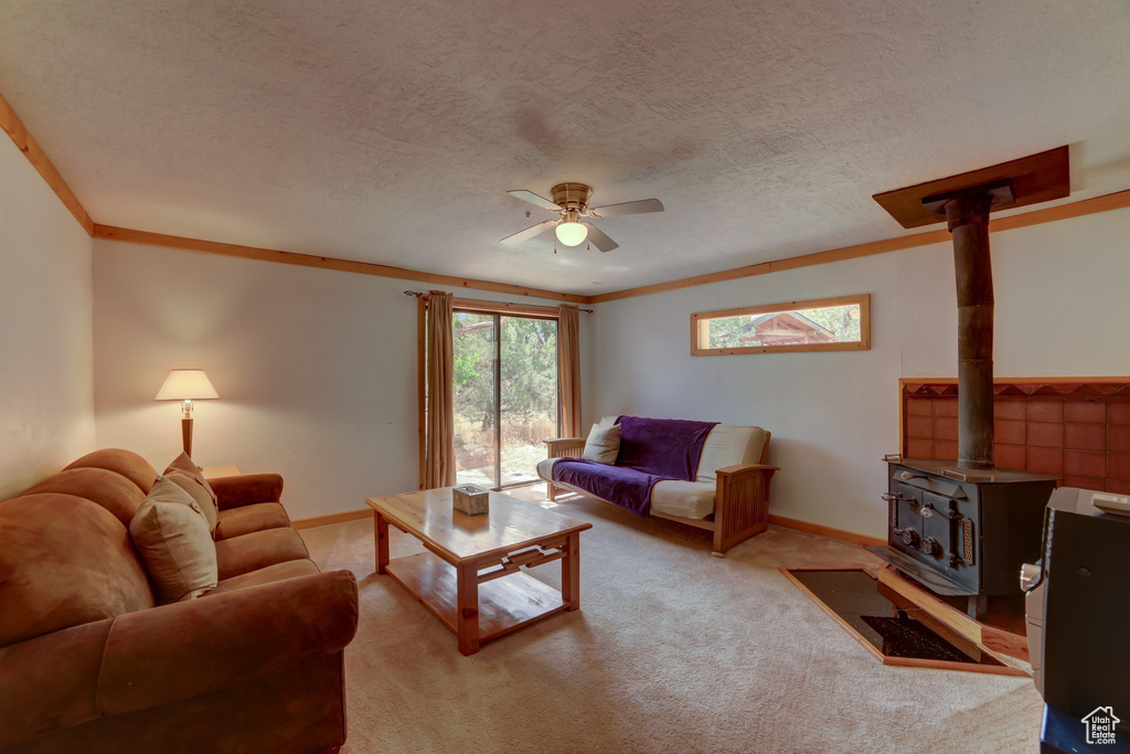 Carpeted living room featuring ornamental molding, ceiling fan, a wood stove, and a textured ceiling