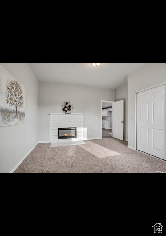 Unfurnished living room featuring a brick fireplace and carpet floors