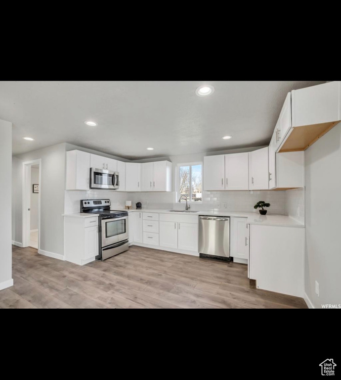 Kitchen featuring stainless steel appliances, tasteful backsplash, white cabinetry, sink, and light wood-type flooring