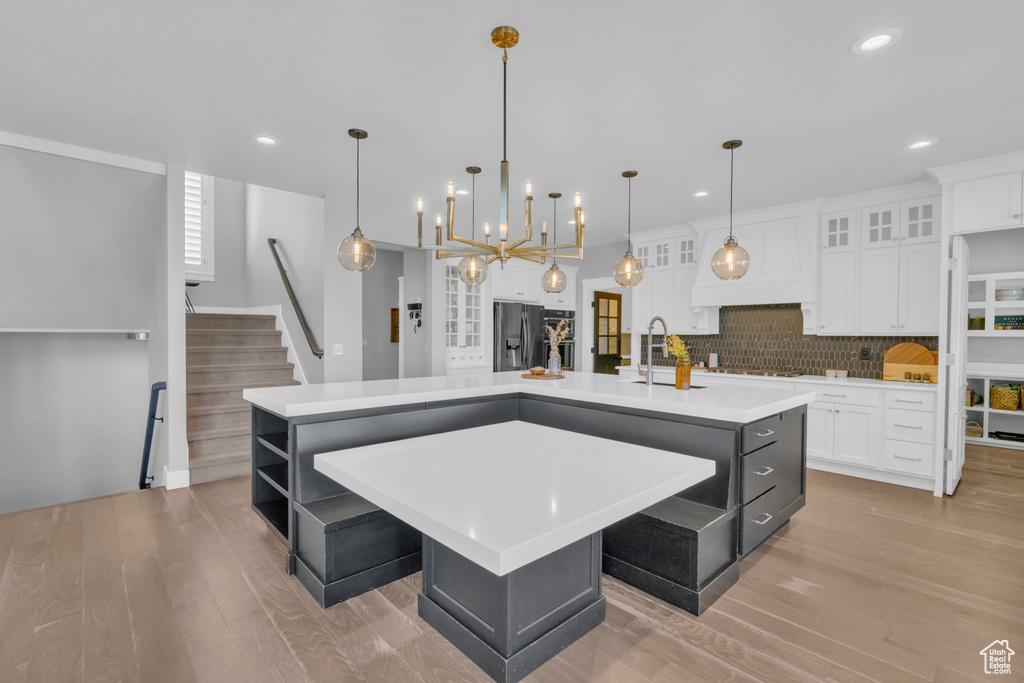 Kitchen with pendant lighting, a kitchen island with sink, light wood-type flooring, tasteful backsplash, and stainless steel fridge