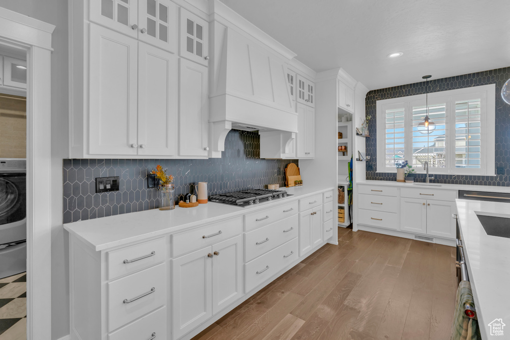 Kitchen featuring hanging light fixtures, premium range hood, tasteful backsplash, and white cabinetry