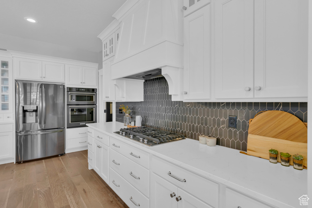Kitchen with backsplash, stainless steel appliances, white cabinets, and light wood-type flooring