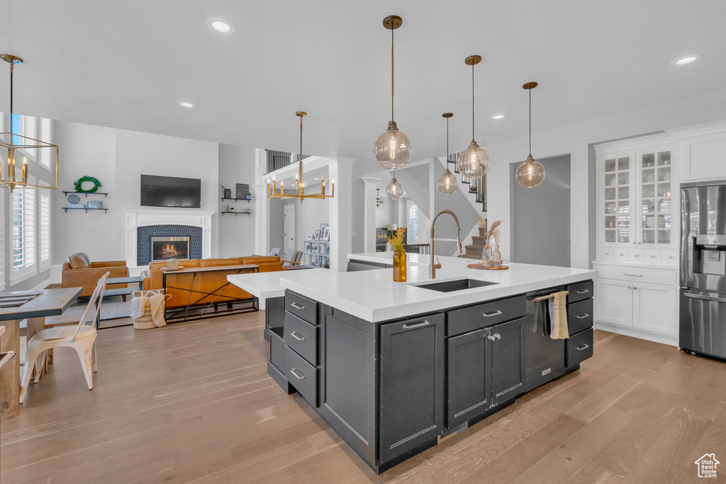 Kitchen featuring pendant lighting, white cabinets, a fireplace, stainless steel refrigerator, and light hardwood / wood-style floors