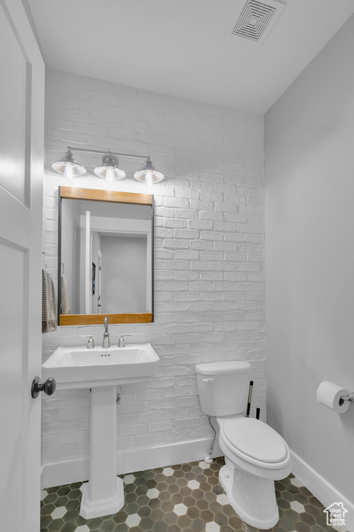 Bathroom with brick wall, toilet, and tile flooring