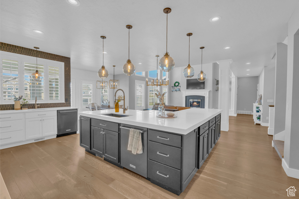 Kitchen featuring hanging light fixtures, light hardwood / wood-style flooring, an island with sink, sink, and stainless steel dishwasher