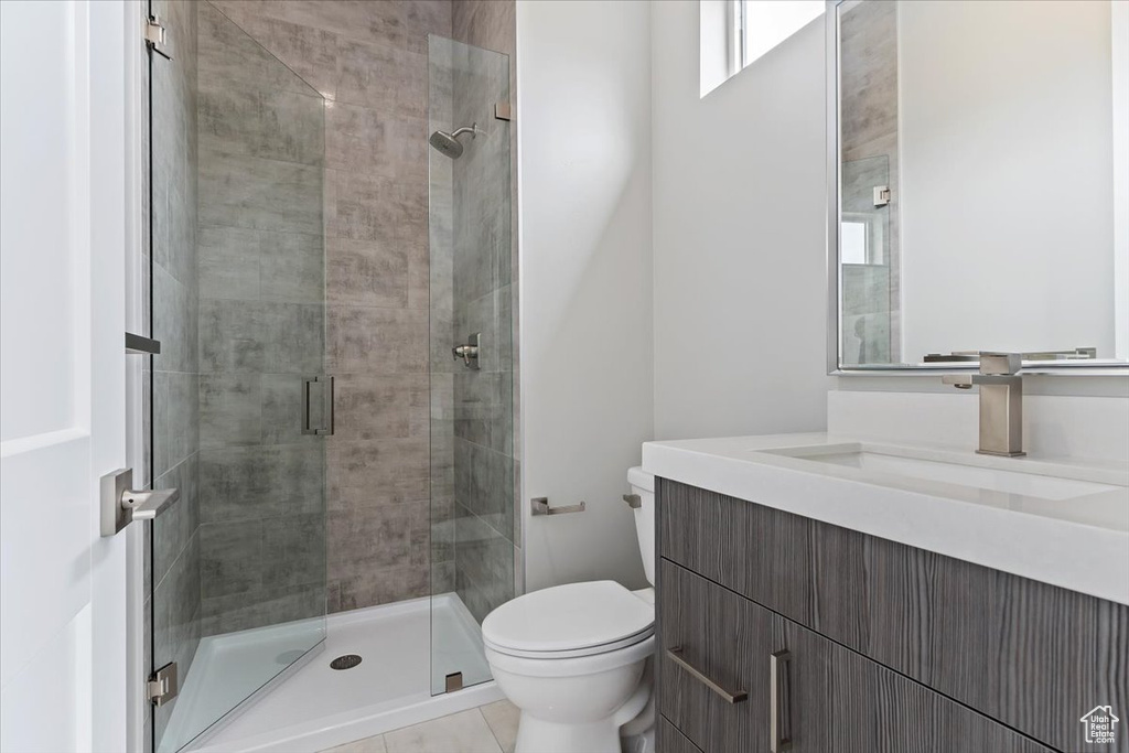 Bathroom with a shower with shower door, vanity, toilet, and tile flooring