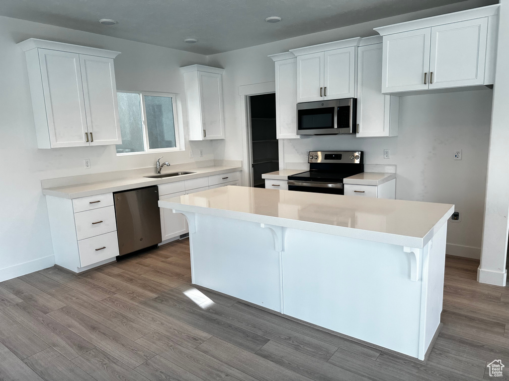 Kitchen featuring a kitchen island, stainless steel appliances, white cabinetry, and a breakfast bar area