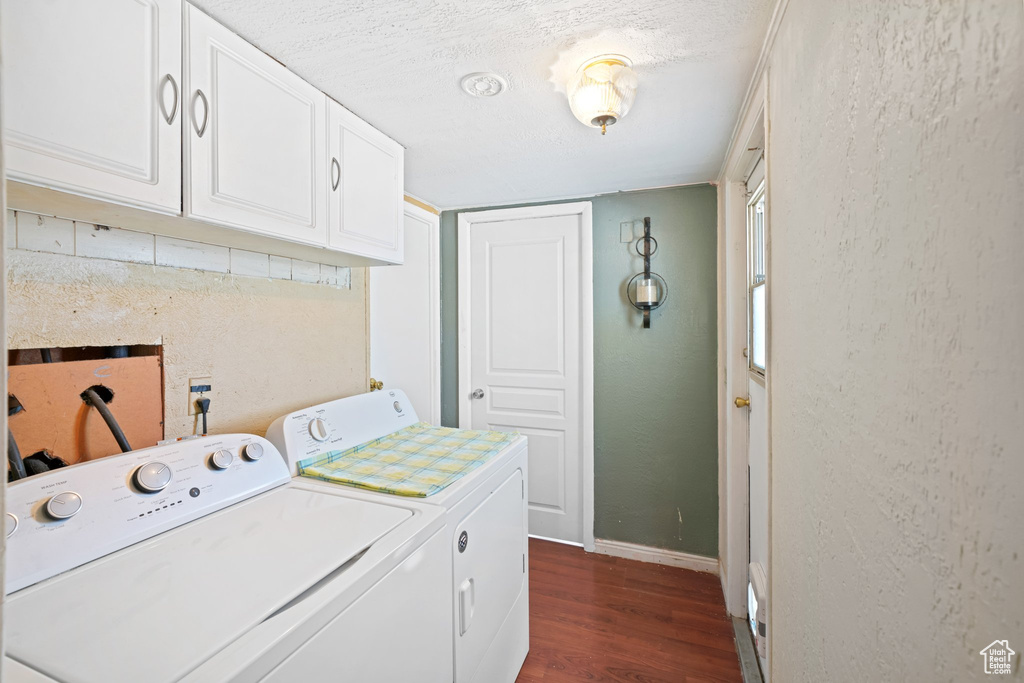 Laundry room with a textured ceiling, cabinets, dark wood-type flooring, and washer and clothes dryer