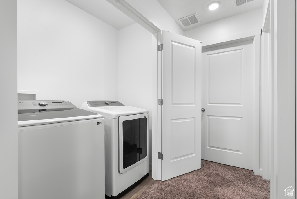 Clothes washing area featuring dark carpet and washing machine and dryer