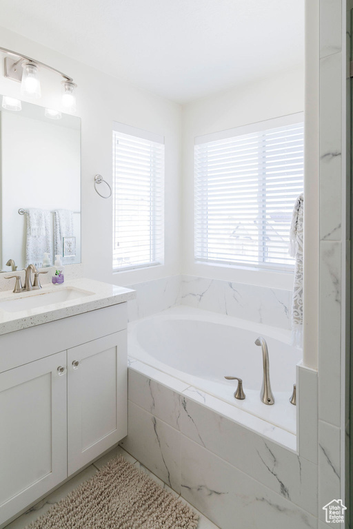 Bathroom featuring a wealth of natural light, a relaxing tiled bath, and large vanity