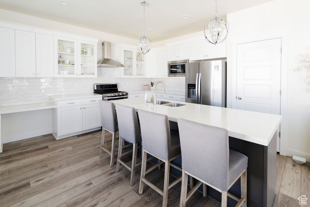 Kitchen featuring light hardwood / wood-style flooring, stainless steel appliances, tasteful backsplash, wall chimney exhaust hood, and sink
