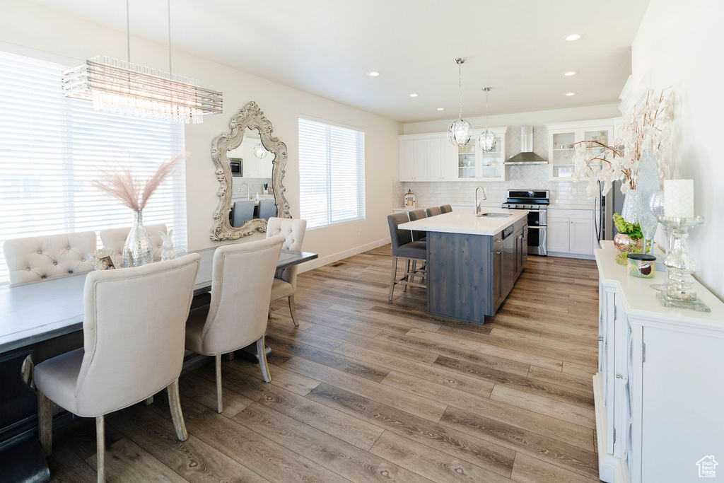 Kitchen featuring tasteful backsplash, hardwood / wood-style flooring, wall chimney range hood, an island with sink, and white cabinets