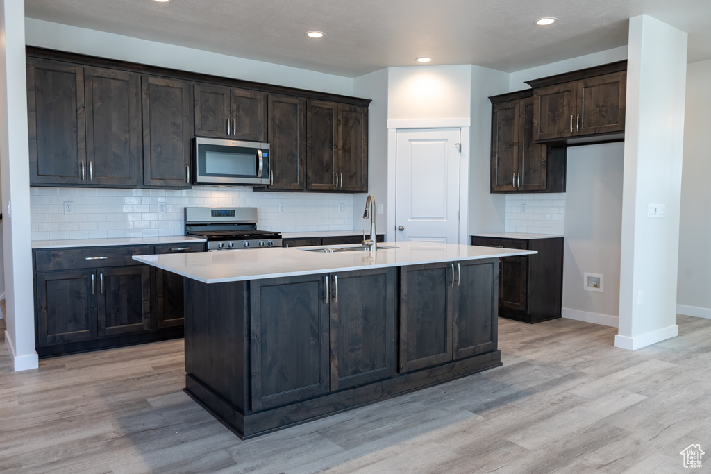 Kitchen featuring a kitchen island with sink, light hardwood / wood-style flooring, stainless steel appliances, sink, and tasteful backsplash