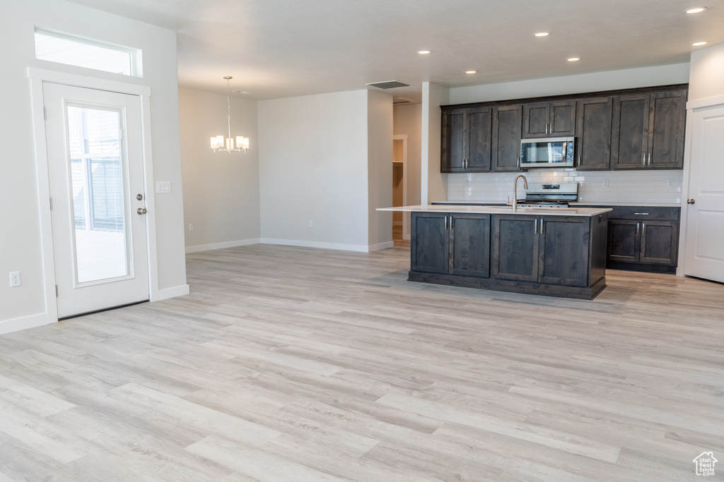 Kitchen with dark brown cabinetry, light hardwood / wood-style floors, backsplash, stove, and pendant lighting